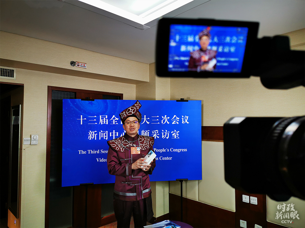 △广西代表团的黄炳辉是全国唯一的毛南族自治县——广西环江县县长。飞机刚落地北京，他就收获了意外之喜：习近平总书记对毛南族实现整族脱贫作出重要指示。在接受总台记者视频采访时，黄炳辉展示了这款产自大山里的智能手机，可帮助5000人就业。（总台央视记者钟陟悦、袁鹏拍摄）
